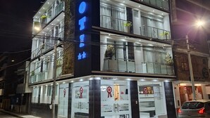 A multi-story hotel with a prominent illuminated sign, balconies with potted plants, and a visible entrance with a red flag. - Hotel Oti (Cajamarca)