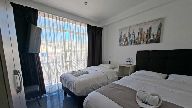 A hotel room with two beds, a painting on the wall, and a view of the city through the window. - Hotel Oti (Cajamarca)