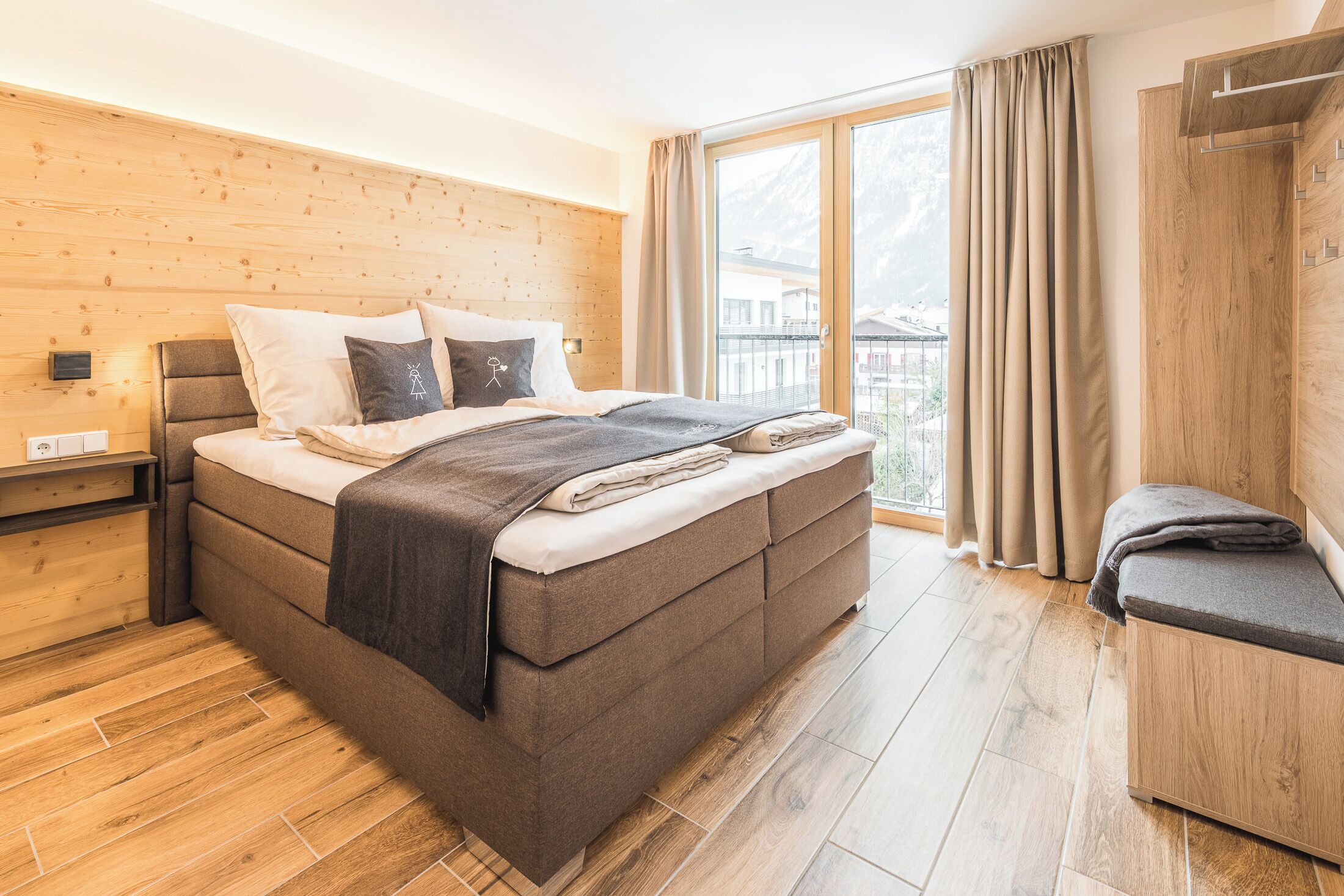 A modern bedroom with a large bed, wooden headboard, and a view of the outdoors.