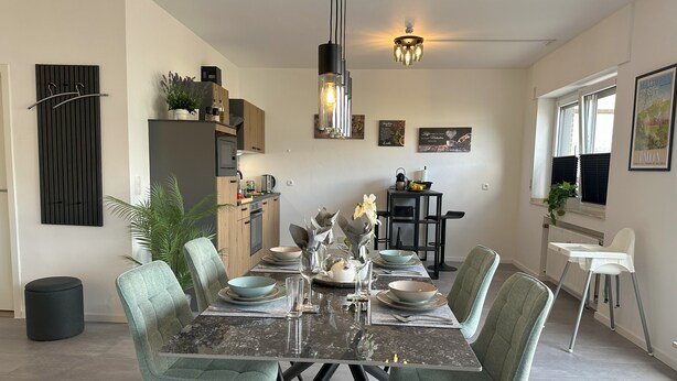 A dining area with a glass-top table, green upholstered chairs, and a black pendant light. - Penthouse, KingSize Bed, Queen Size SofaBed, full Kitchen, 650 MBit, Workspace (Euskirchen)
