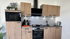 A modern kitchen with wooden cabinets, a black microwave, a stove, and a sink. - Penthouse, KingSize Bed, Queen Size SofaBed, full Kitchen, 650 MBit, Workspace (Euskirchen)