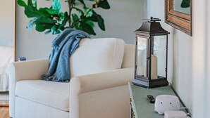 A room with a white armchair, a green side table with a lantern, a potted plant, and a wall-mounted TV. - The Guest Wing at Kateri: Luxury Stay Waynesboro (Waynesboro)