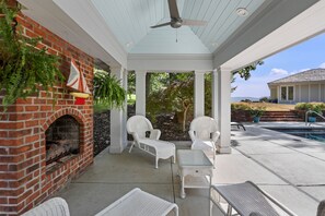 A covered patio with a brick fireplace, white wicker furniture, and a pool in the background. - The Guest Wing at Kateri: Luxury Stay Waynesboro (Waynesboro)