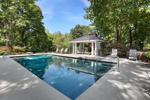Une piscine rectangulaire agrémentée d’un kiosque, de chaises longues et d’une terrasse dallée.