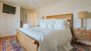 A bedroom with a wooden bed, a ceiling fan, a TV mounted on the wall, and a bedside lamp. - The Guest Wing at Kateri: Luxury Stay Waynesboro (Waynesboro)