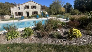 Una casa de piedra con piscina, rodeada de plantas y árboles.