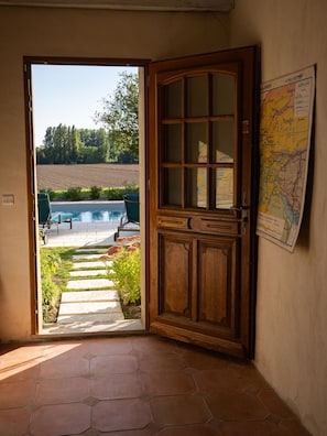 A room with a wooden door leading to a pool area, a map on the wall, and a tiled floor. - Charming 300m2 house in stones, can accomodate up to 12 persons. Private pool. (Pardaillan)