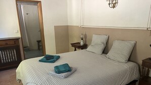 Una cama bien hecha con ropa de cuadros, una mesita de noche con lámpara y un espejo en la pared.