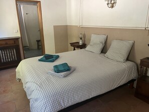 A neatly made bed with checkered bedding, a bedside table with a lamp, and a mirror on the wall. - Charming 300m2 house in stones, can accomodate up to 12 persons. Private pool. (Pardaillan)