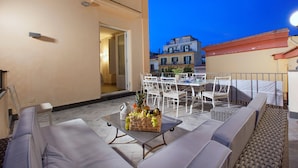 Eine Terrasse im Freien mit Esstisch, Stühlen und einer Obstschale.