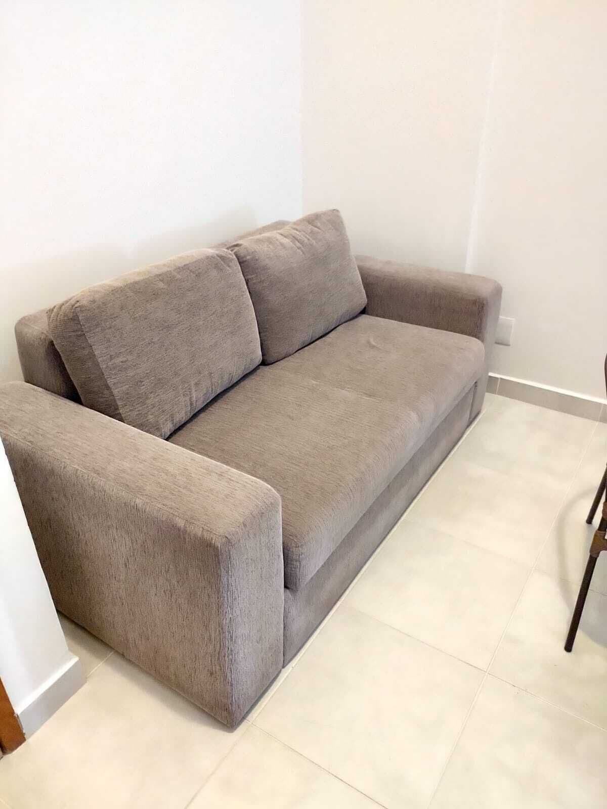 A grey sofa with a wooden armrest in a room with white walls and tiled flooring.