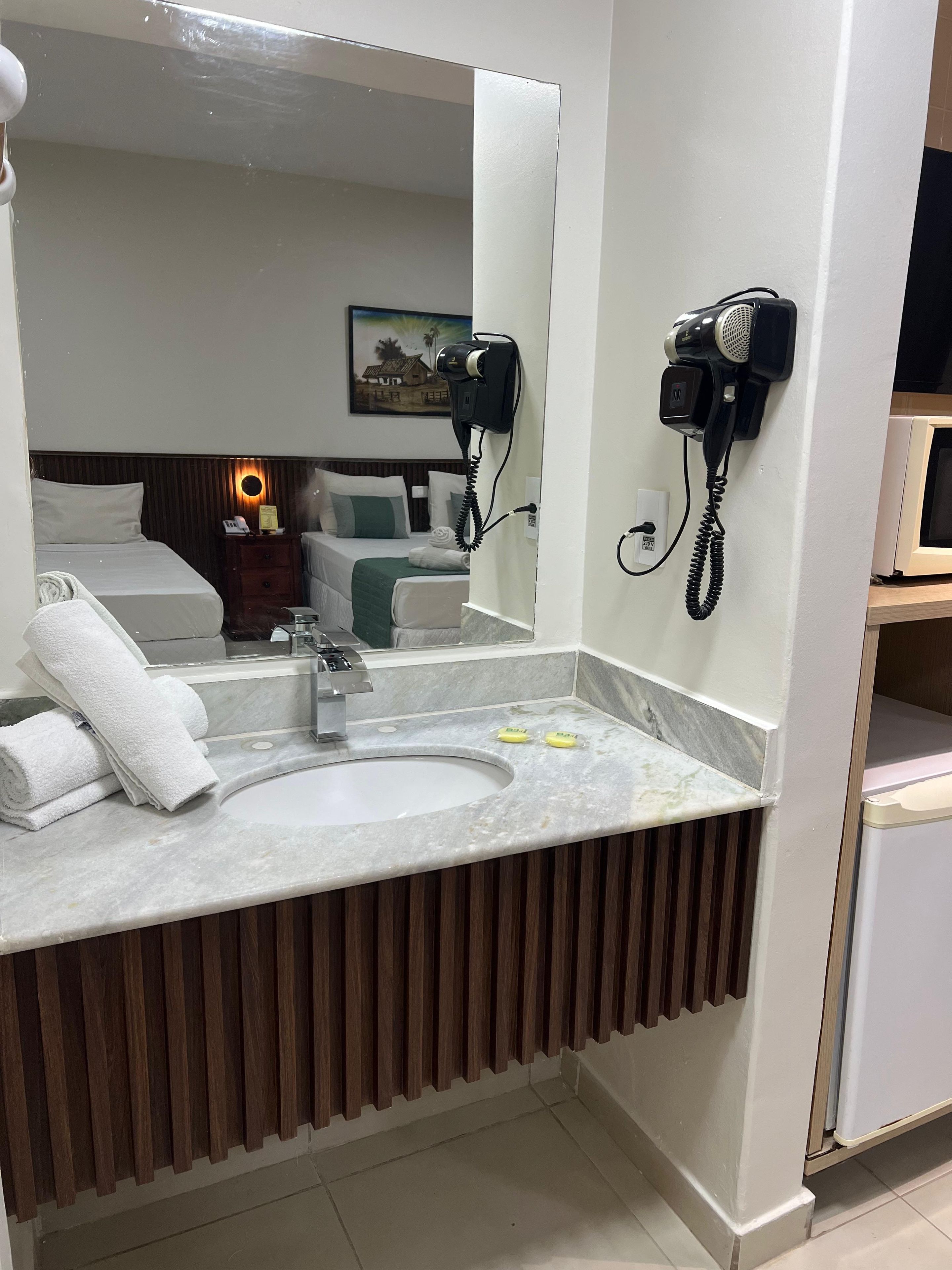 A hotel bathroom with a marble sink, a mirror, a hair dryer mounted on the wall, and a towel rack with folded towels.