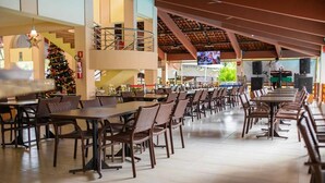 A spacious indoor dining area with multiple tables and chairs, a Christmas tree, and a television screen. - Hot Springs Flat Apart Hotel c. Banheira (Caldas Novas)
