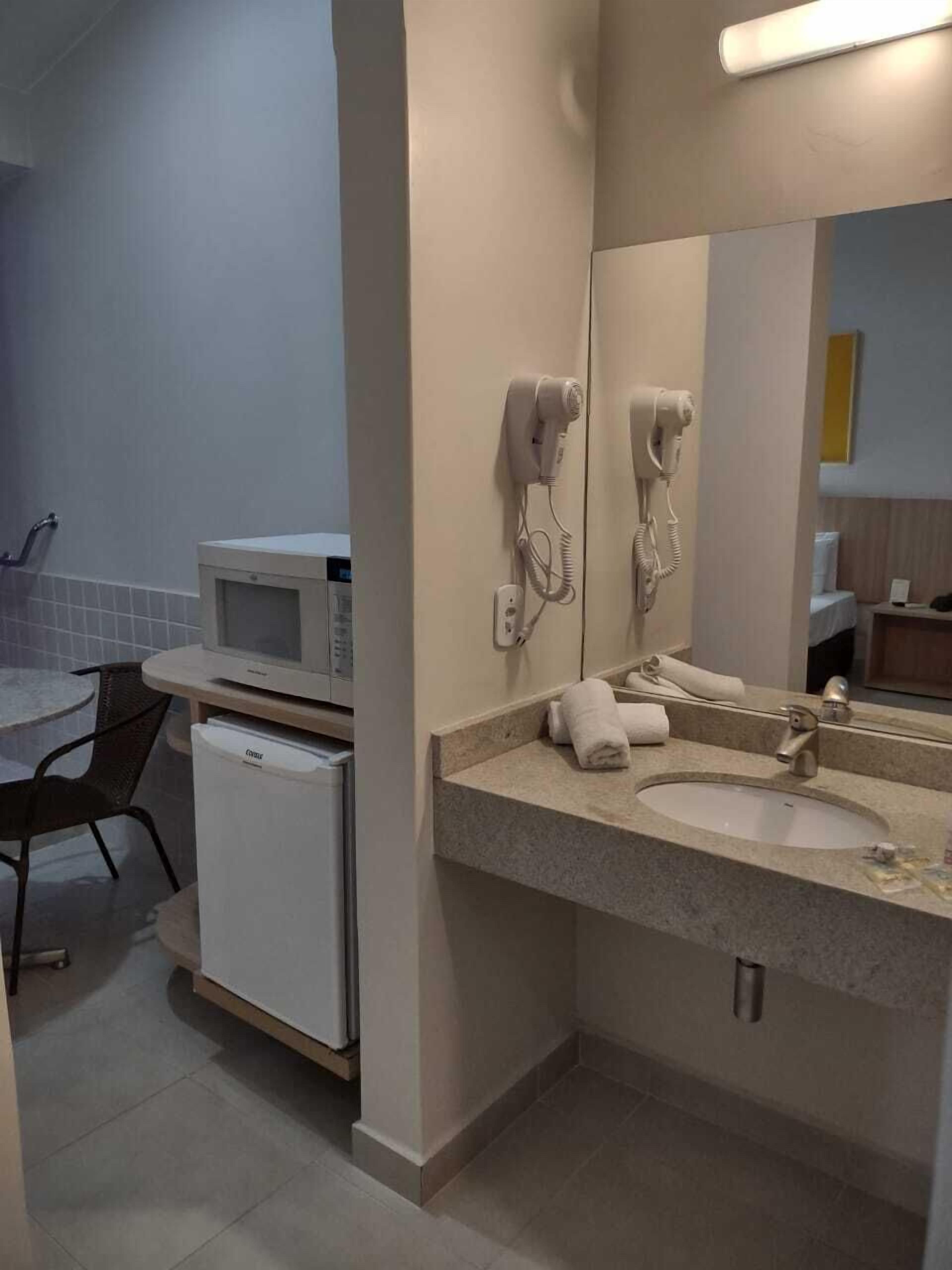 A compact hotel bathroom with a sink, mirror, hairdryer, and microwave.