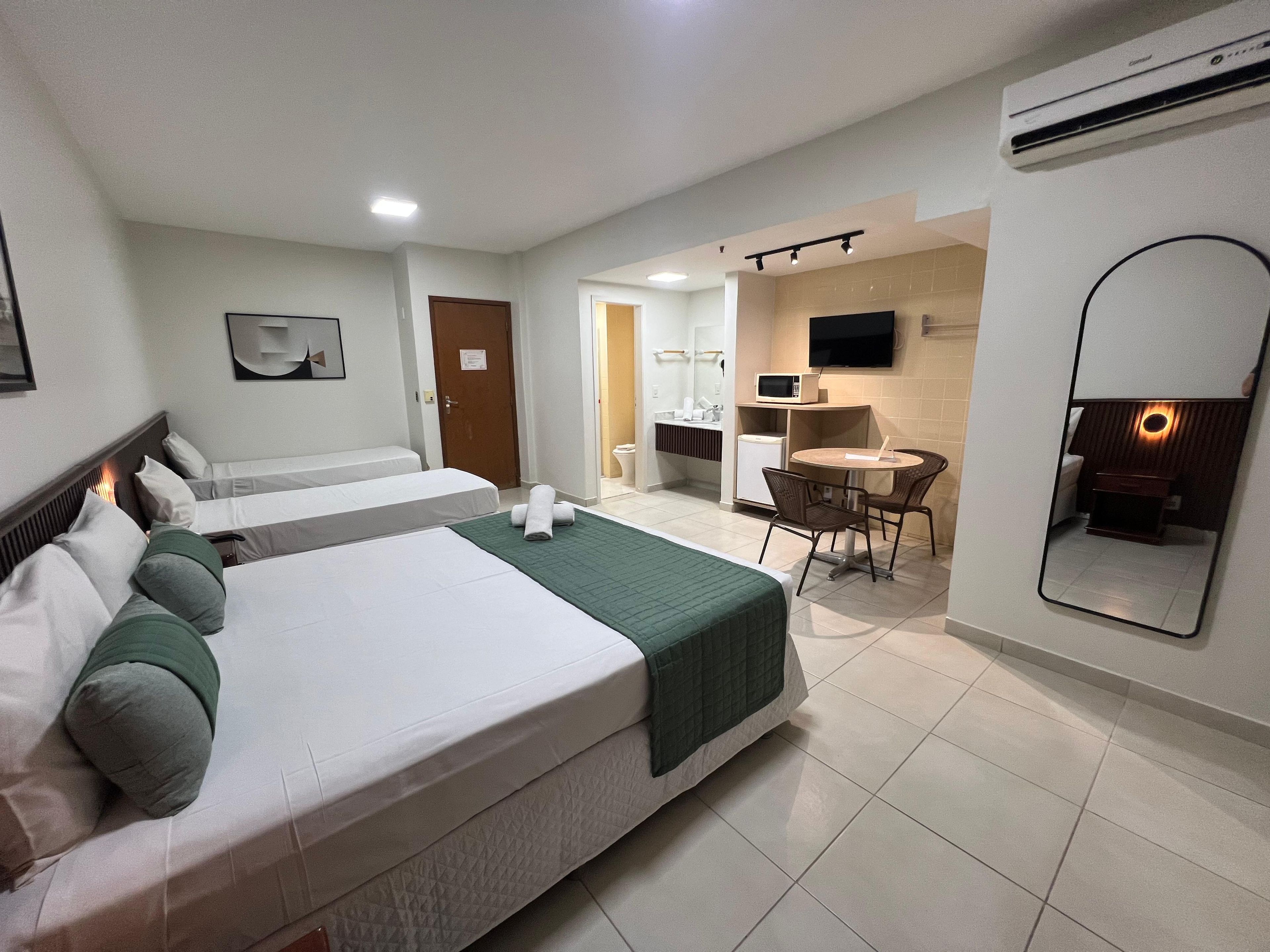Habitación de hotel con dos camas, una sala de estar con una mesa y sillas, microondas, televisión y aire acondicionado.