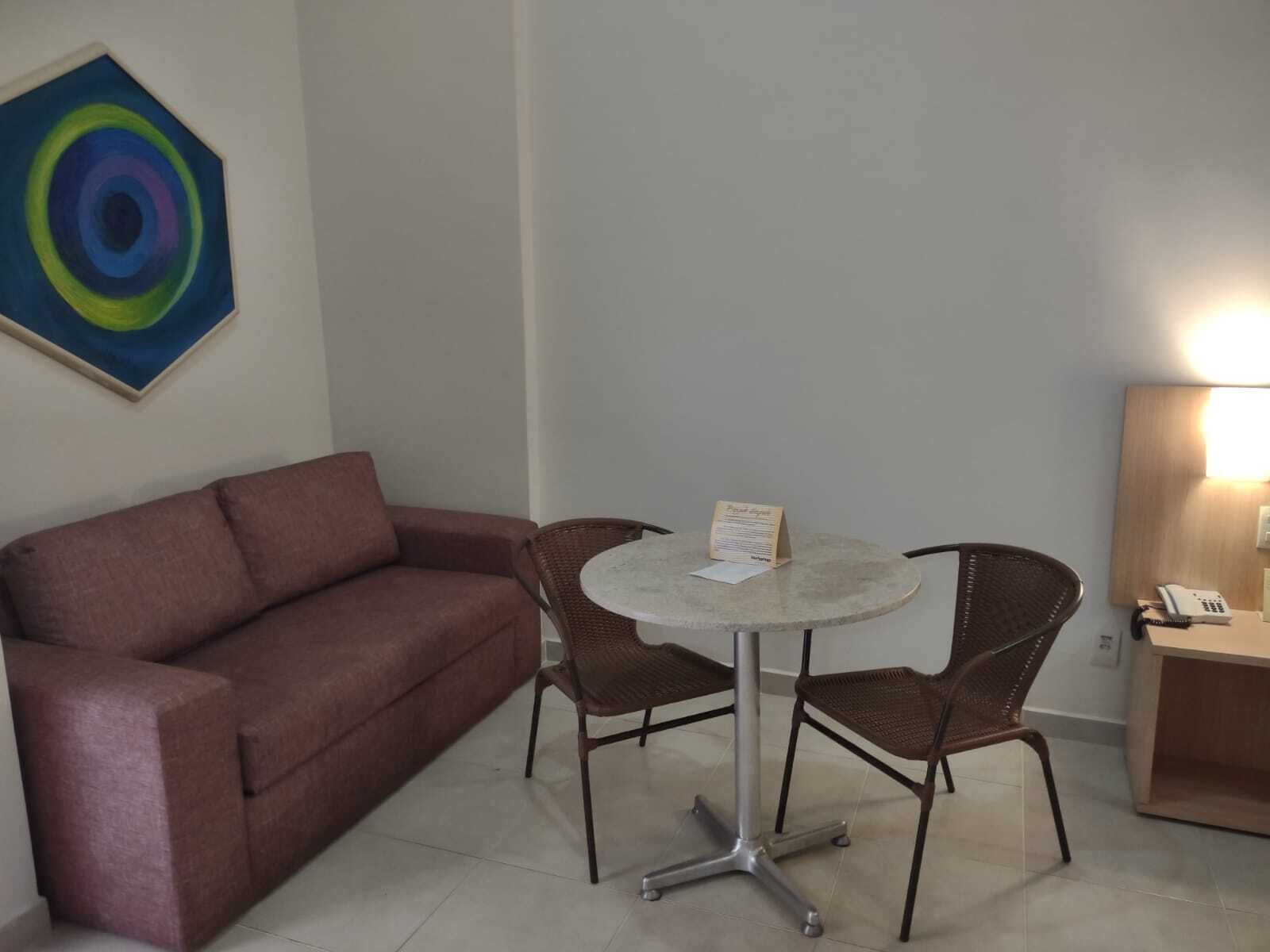 A room with a brown sofa, two wicker chairs, a small round table, and a painting on the wall.