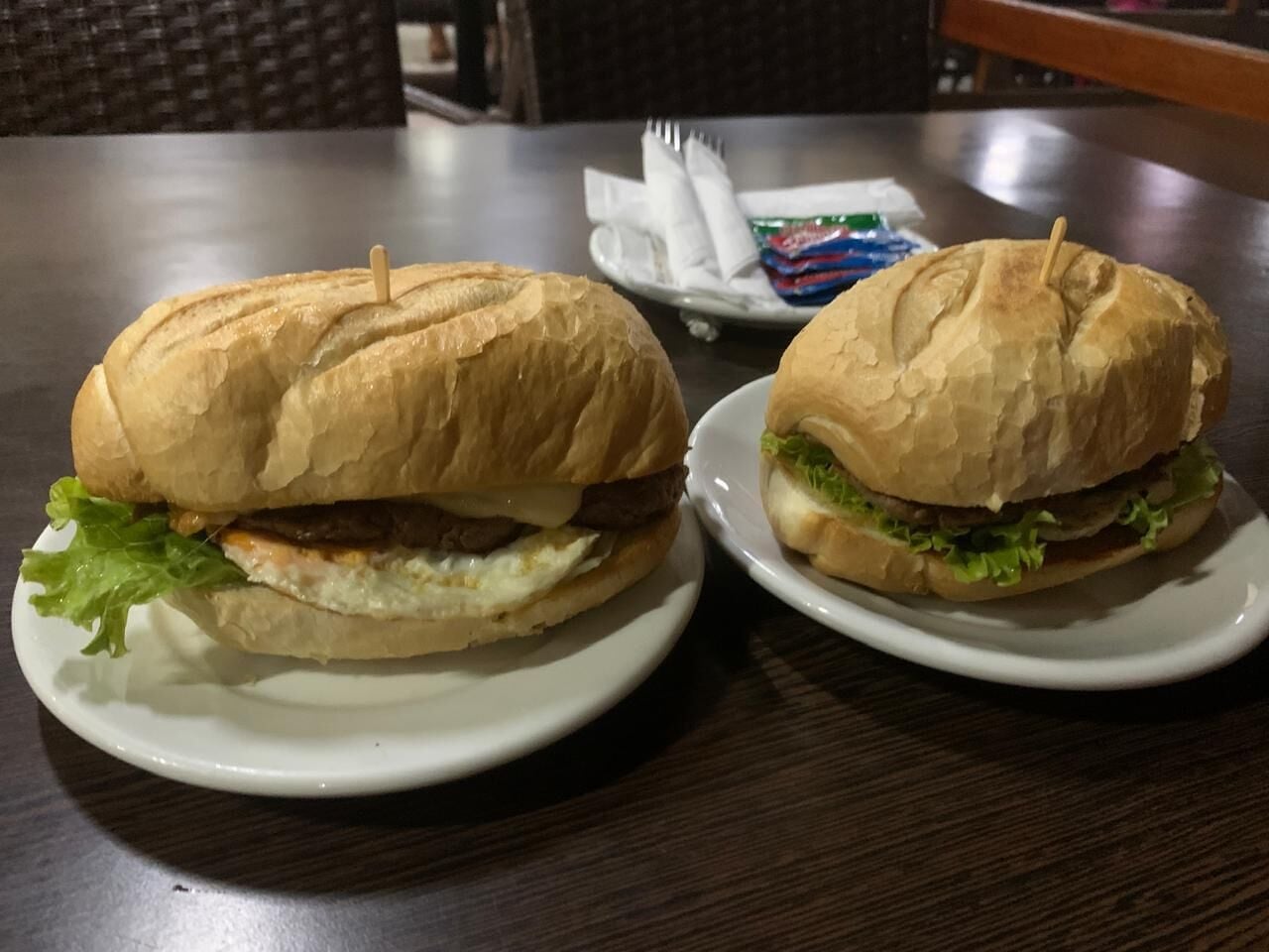 Two sandwiches on white plates on a wooden table.