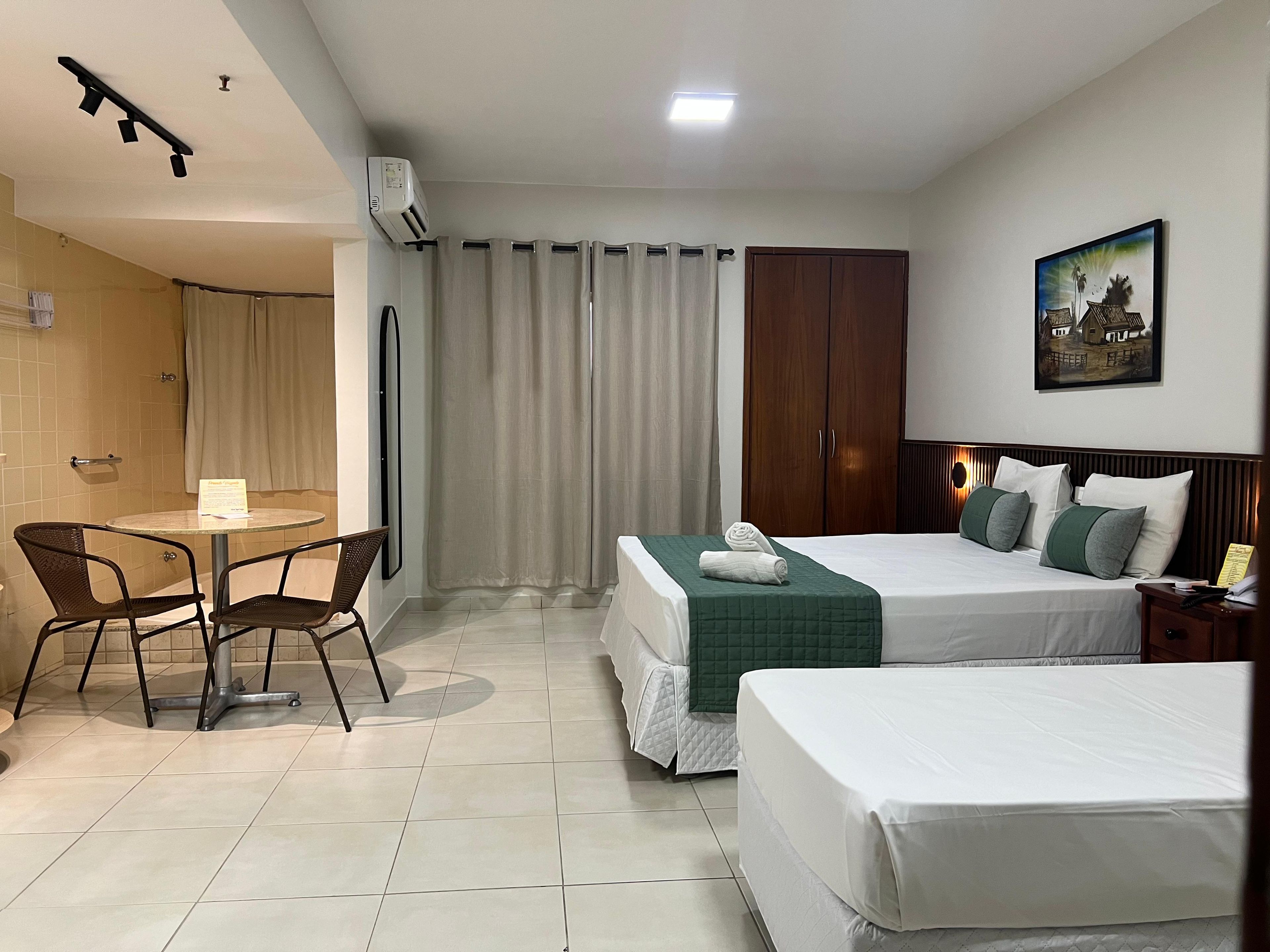A hotel room with a bed, a desk with chairs, a wardrobe, and a painting on the wall.
