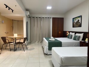 A hotel room with a bed, a desk with chairs, a wardrobe, and a painting on the wall. - Hot Springs Flat Apart Hotel c. Banheira (Caldas Novas)