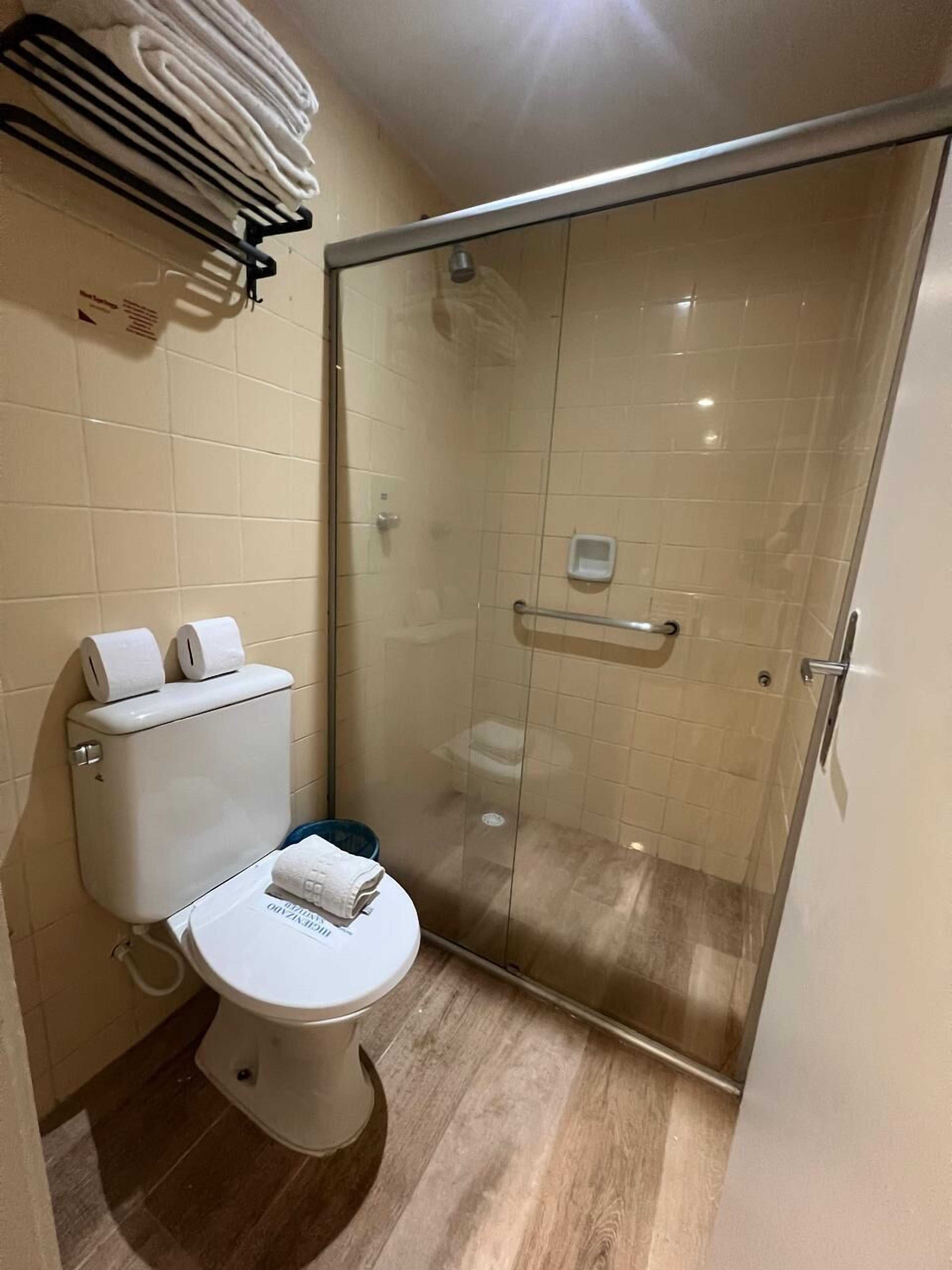 Ein Badezimmer mit Toilette, einer Duschkabine aus Glas und einem Handtuchhalter mit gefalteten Handtüchern.
