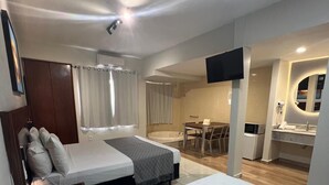 A modern hotel room with a large bed, a desk, a chair, a TV, and a bathroom with a mirror and sink. - Hot Springs Flat Apart Hotel c. Banheira (Caldas Novas)