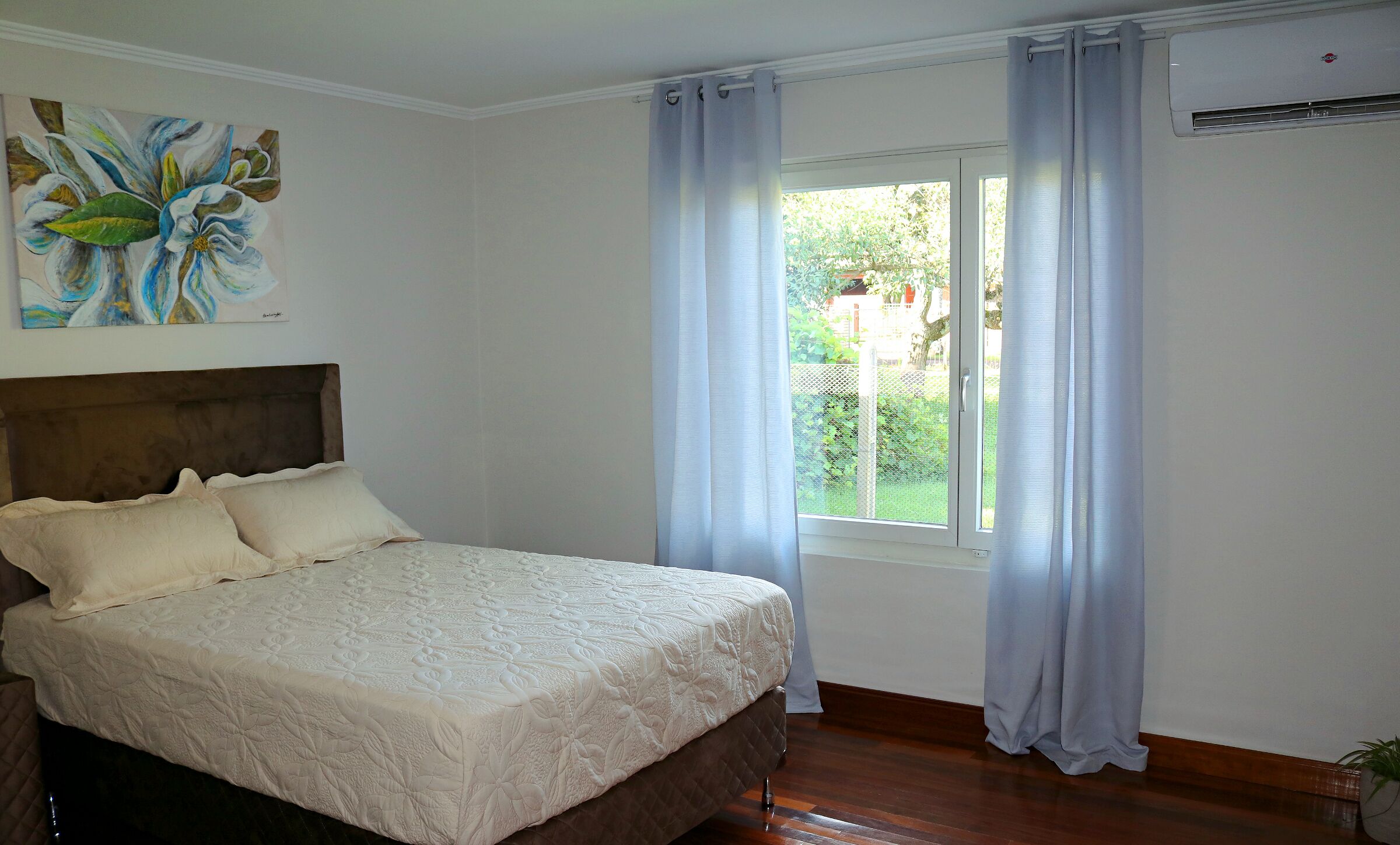 A bedroom with a bed, a headboard, a window with curtains, and a painting on the wall.