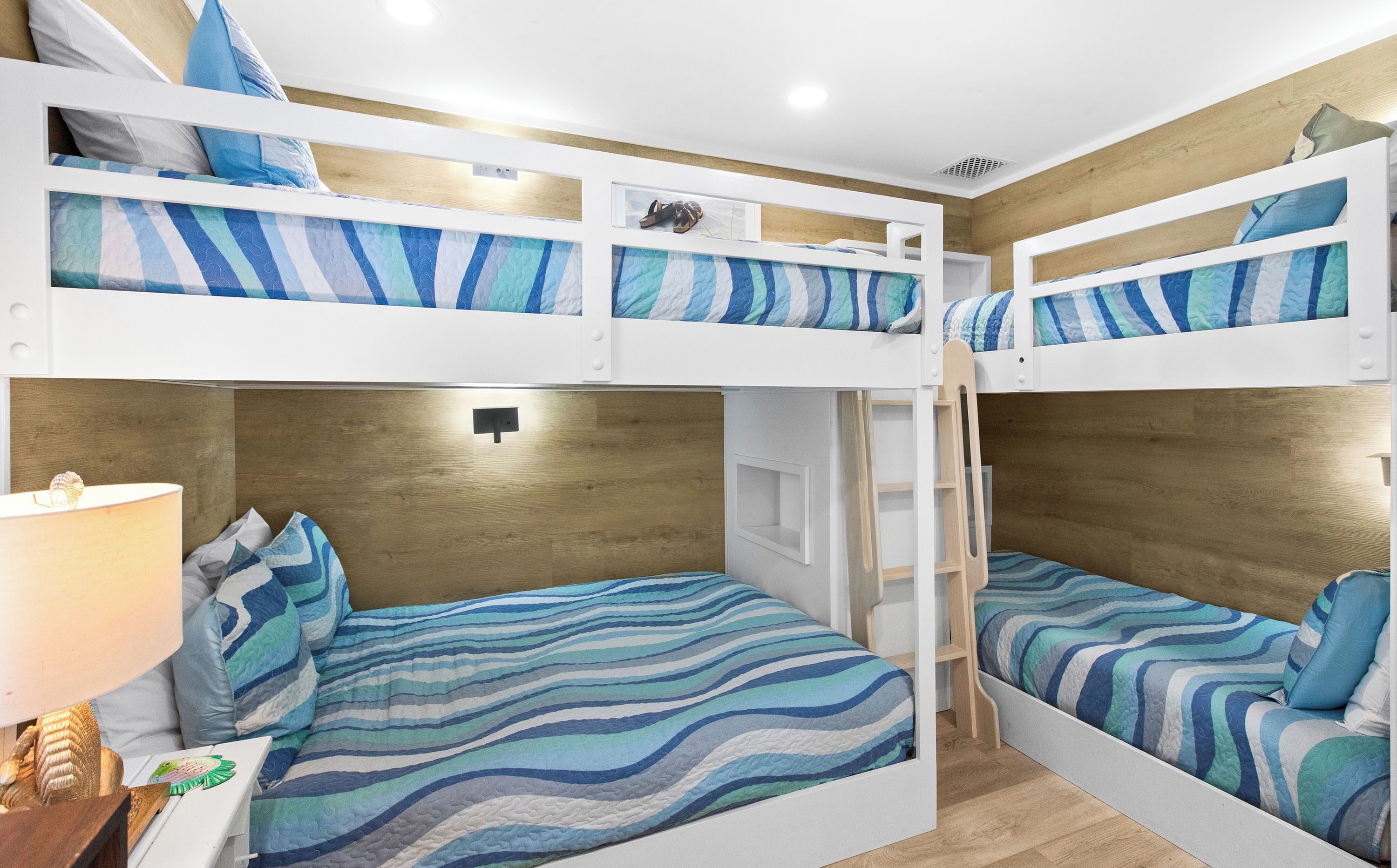 A bunk bed room with striped bedding, a nightstand, and a lamp.