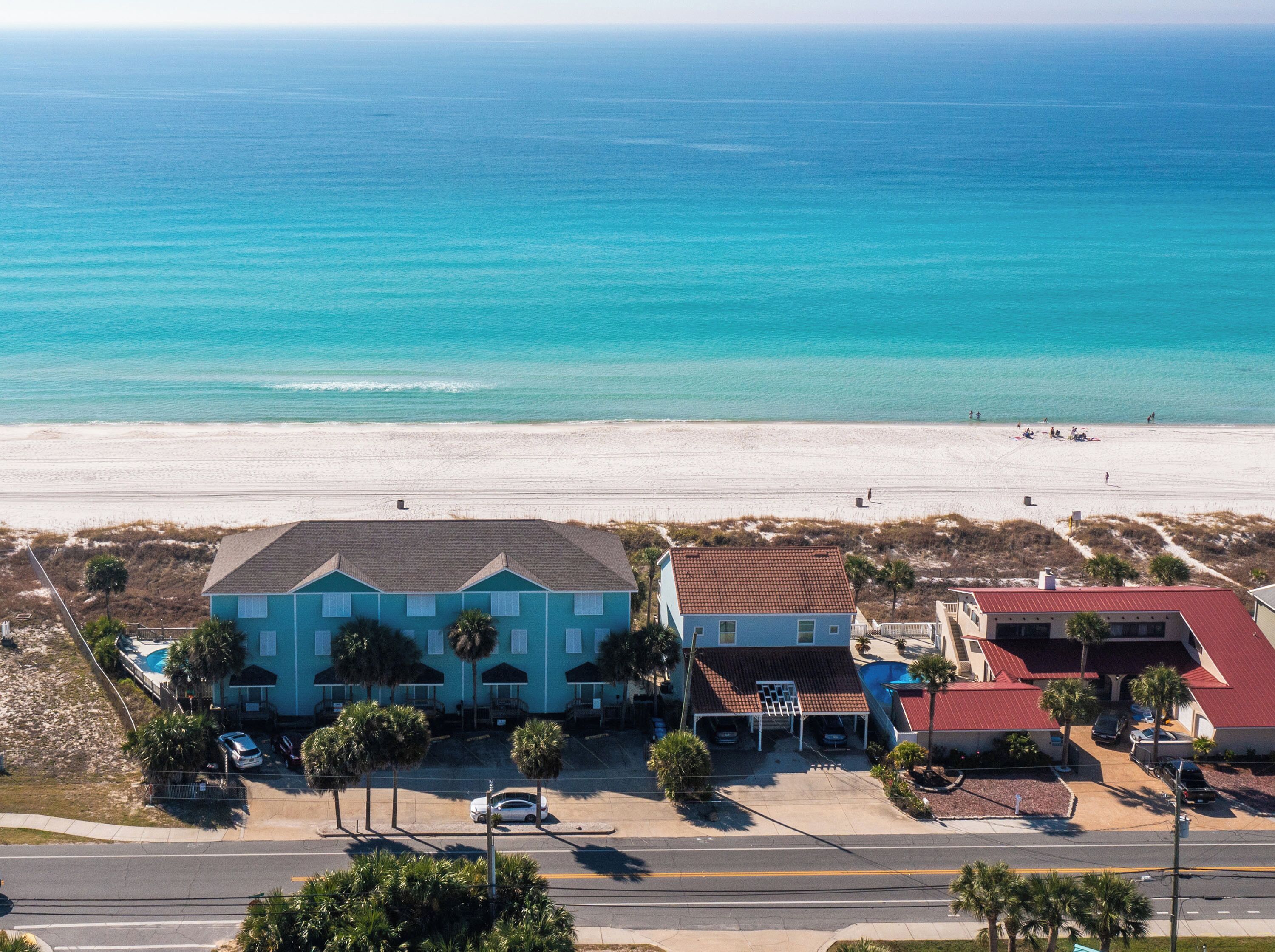 A coastal hotel with a beach view, featuring a main building with a red roof and a smaller adjacent structure.
