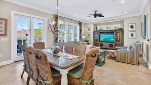 A spacious dining area with wicker chairs and a glass-top table, a cozy seating area with a sofa and armchairs, and a television in the background. - Grits-Carlton: Private beach steps away, Heated pool, Bunk rooms, Lakefront view (Miramar Beach)