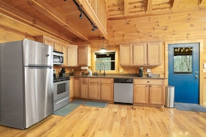 A modern kitchen with wooden cabinets, stainless steel appliances, and a blue door. - Goat Run Retreat | Hocking Hills, Hot Tub, Sauna (Logan)