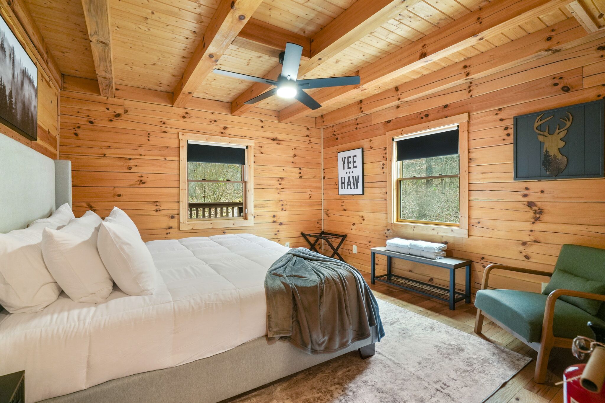 Une chambre dans une cabane en bois, avec un lit, une chaise, une table et un ventilateur de plafond.