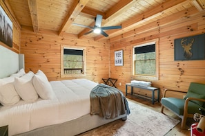 A wooden cabin bedroom with a bed, a chair, a table, and a ceiling fan. - Goat Run Retreat | Hocking Hills, Hot Tub, Sauna (Logan)