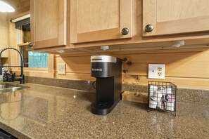 A kitchen with wooden cabinets, a Keurig coffee maker, a sink, and a coffee pod holder. - Goat Run Retreat | Hocking Hills, Hot Tub, Sauna (Logan)