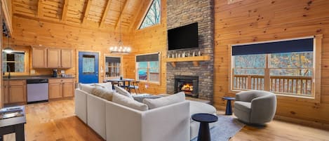A spacious living area with a fireplace, wooden walls, and a large window overlooking a deck.