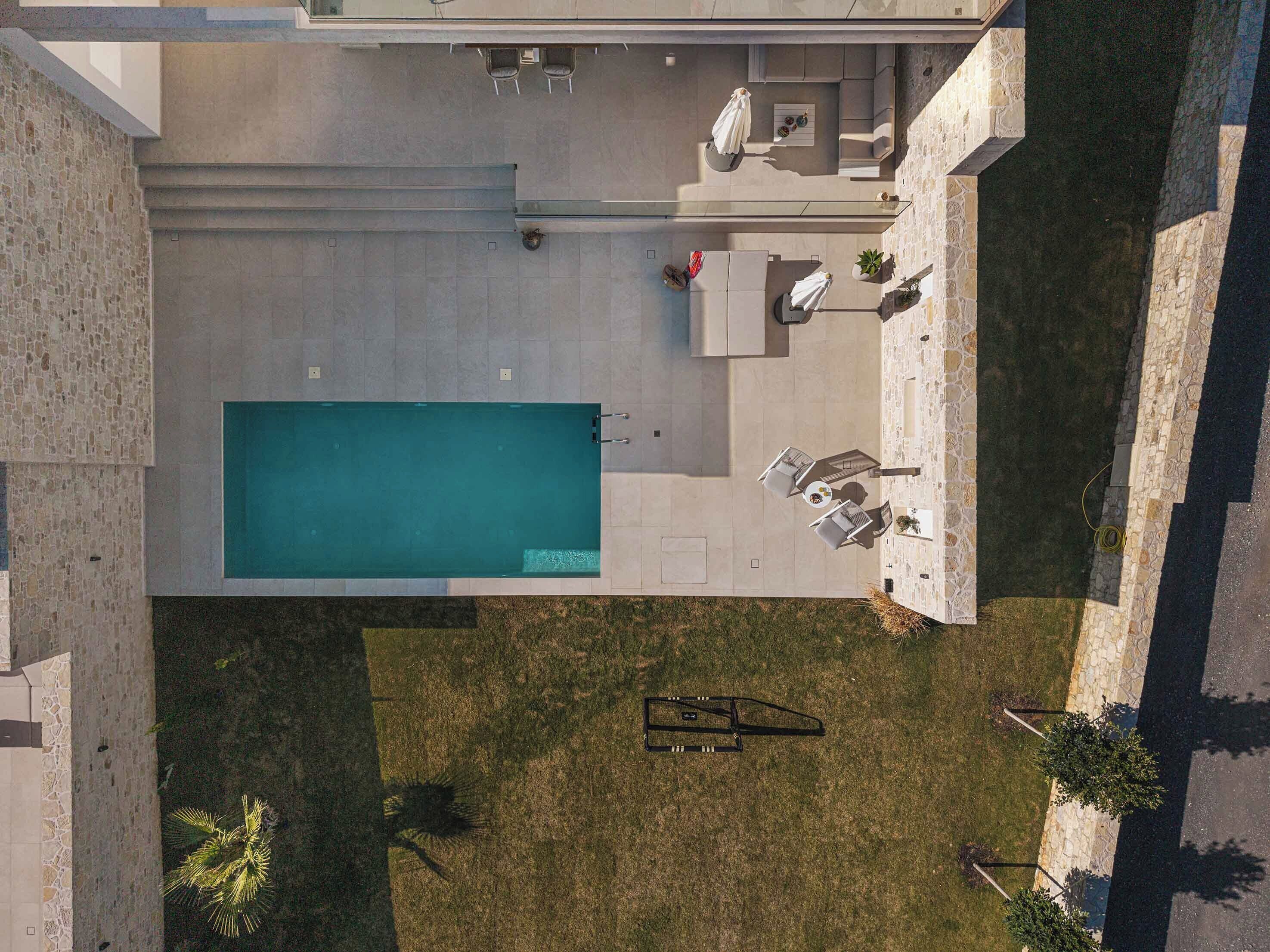 An aerial view of a residential property with a swimming pool, outdoor seating area, and a small garden.