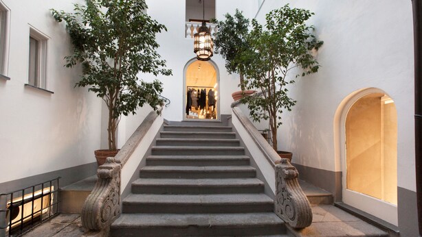 A staircase with ornate balustrades, flanked by potted trees, leading to a warmly lit interior space. - Palazzo Mary in Sorrento (Sorrento)