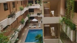 Ein mehrgeschossiges Atrium mit einem zentralen Pool, Balkonen mit Bepflanzung und Sitzbereichen im Freien.