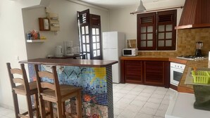 A kitchen with a tiled island, wooden chairs, a microwave, a refrigerator, and a stove.
