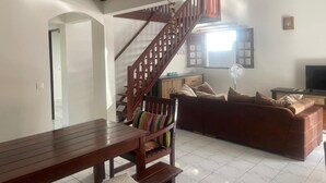 A living room with a wooden staircase, a brown sofa, a wooden dining table, and a TV.