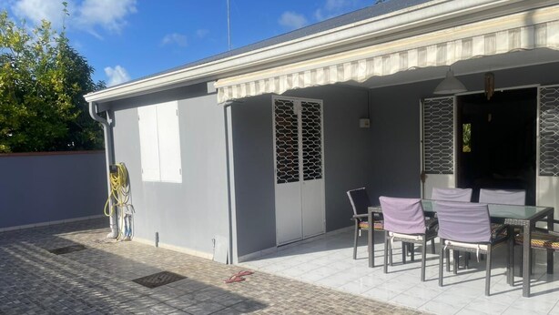 A covered outdoor seating area with a table and chairs, a door with a decorative grille, and a power outlet on the wall.