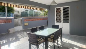 A covered patio with a glass-top table and chairs, a ceiling fan, and a view of the outside.