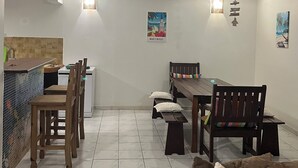 A dining area with a wooden table and chairs, a bench, a sofa, and a kitchen area with a tiled backsplash and a sink.