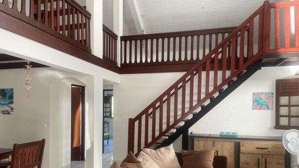 A spacious living area with a wooden staircase, a sofa set, and a dining table.