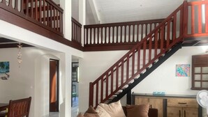 A spacious living area with a wooden staircase, a sofa set, and a dining table.