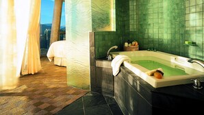 Une salle de bain moderne avec une grande baignoire, des murs recouverts de carreaux verts et une vue sur le paysage urbain, visible à travers une grande fenêtre.
