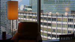 Une chambre d’hôtel dotée d’une grande fenêtre donnant sur un paysage urbain, avec notamment un immeuble arborant le drapeau canadien.