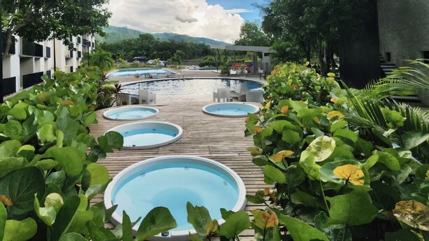 Et poolområde med flere runde pools omgivet af frodig vegetation og et bjerglandskab.