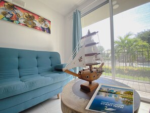 Ein Zimmer mit einem blauen Sofa, einem hölzernen Schiffmodell und einem Poster auf einem runden Tisch.