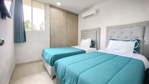 Et hotelværelse med to senge, et vindue med gardiner, en aircondition samt et flisegulv.