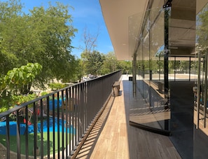 Ein Balkon mit Blick auf einen Swimmingpool und Bäume, eine Glasdoor und ein Holzboden.